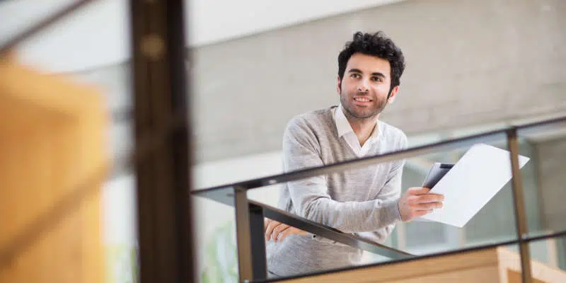 Man used for Values and Public Policy course leaning on railing holding iPad and paper