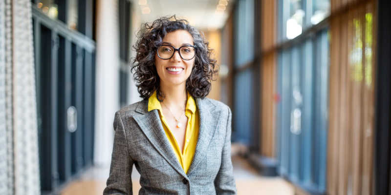 Woman used for Evidence in Public Policy course in glasses and grey jacket smiling at the camera