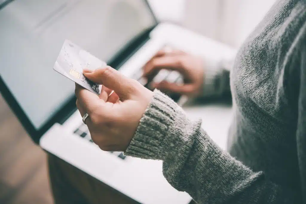 hand holding credit card in front of laptop