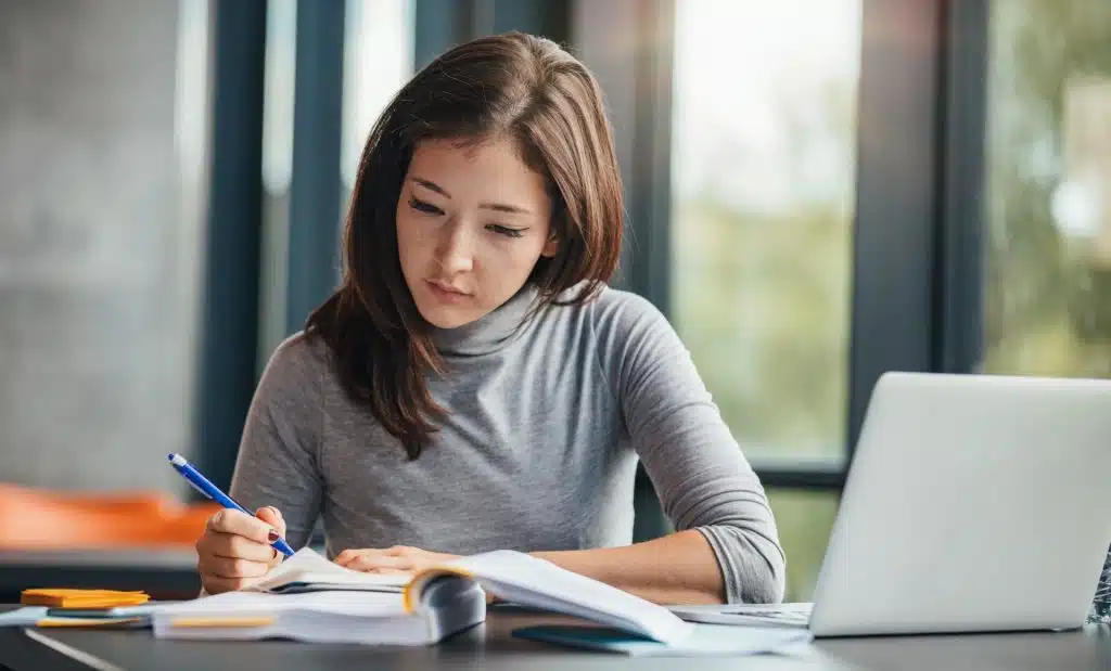 Woman studying PhD in public policy at table with laptop writing notes