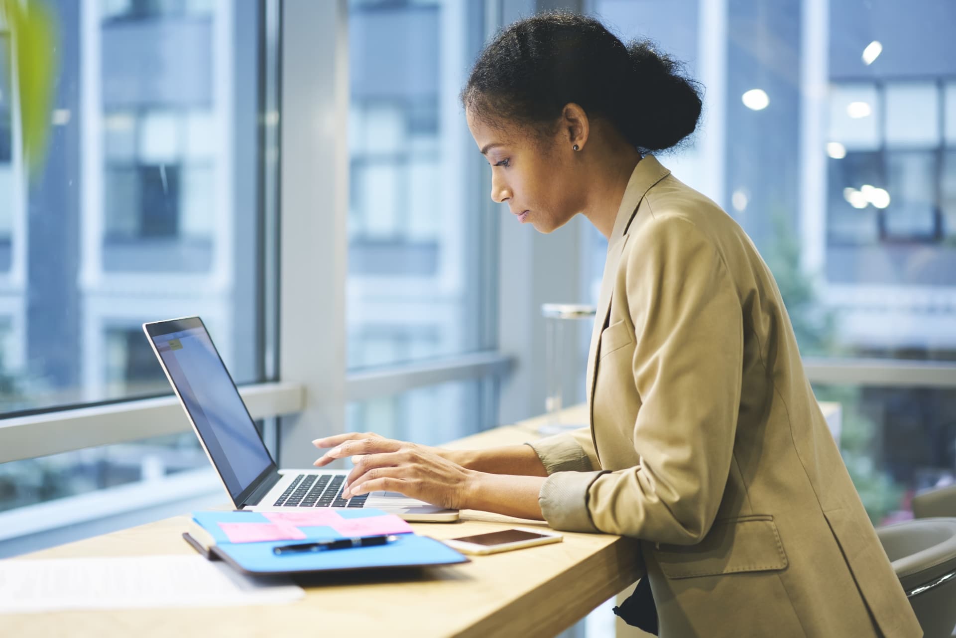 smartly dressed woman typing on laptop in front of window reading about public policy learning methods.